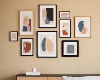 Composición de cuadros y láminas enmarcadas sobre pared color arena en living contemporáneo